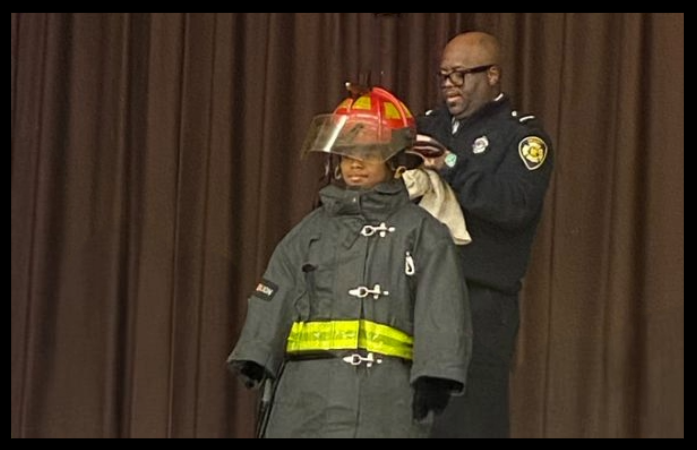 student trying on fire gear helped by fire fighter